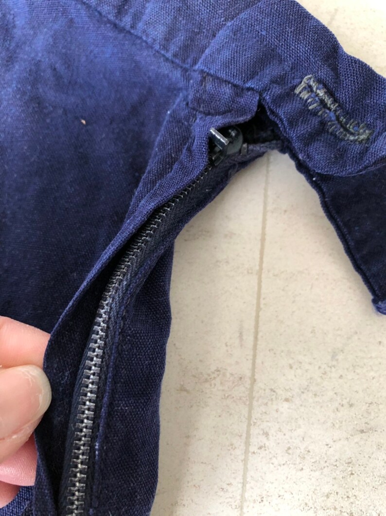 May include: Close-up of a navy blue zipper on a garment. The zipper is metal and has a black pull tab.