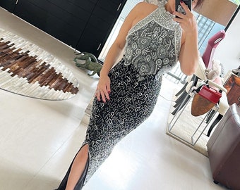 Può includere: Un abito da sera nero e argento con paillettes, con scollo halter e uno spacco laterale. L'abito è lungo fino ai piedi e ha una silhouette aderente.