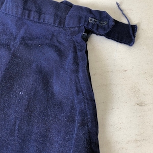 May include: Close-up of the top of a dark blue skirt with a zipper and a button closure.
