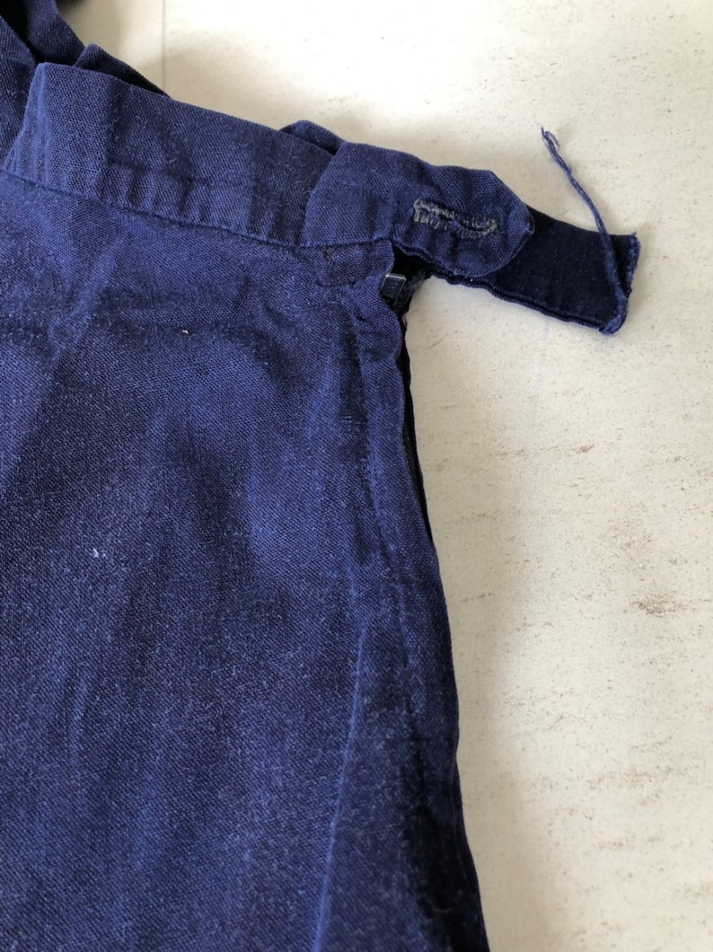 May include: Close-up of the top of a dark blue skirt with a zipper and a button closure.