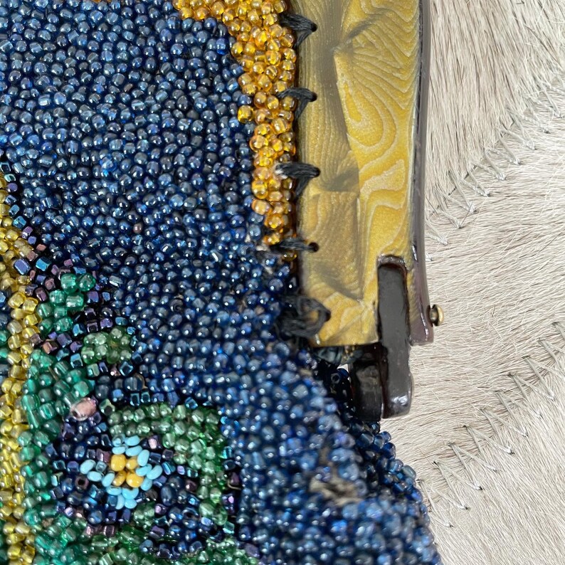 May include: Close-up of a beaded purse with a blue, green, and yellow floral pattern. The purse has a gold-toned clasp and a black drawstring.
