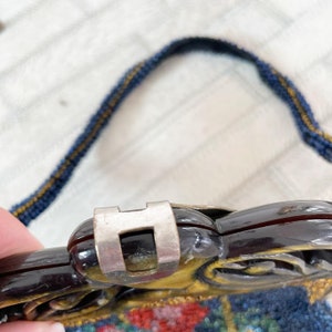 May include: Close-up of a vintage beaded purse with a black and gold floral design. The purse has a metal clasp and a dark brown handle.