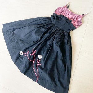 May include: A black and red gingham dress with a black skirt and a white floral embroidery detail. The dress has thin straps and a fitted bodice.