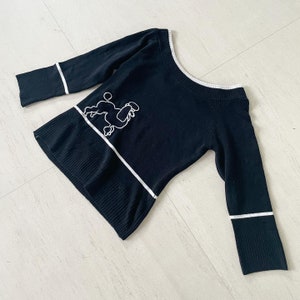 Könnte beinhalten: Schwarzer Pullover mit einem weißen Pudel-Design und weißen Besatz an Ausschnitt und Ärmeln.