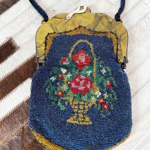 May include: A vintage beaded purse with a floral design. The purse is blue with gold accents and features a basket of flowers with red, pink, and white blooms.