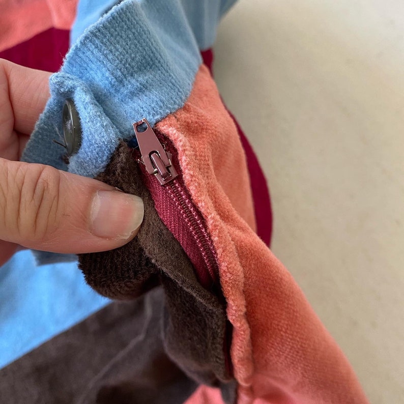 May include: Close-up of a multi-colored fabric with a zipper. The fabric is a mix of brown, blue, pink, and red.