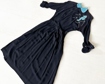 May include: A black dress with a blue velvet collar and a design of birds on the front.