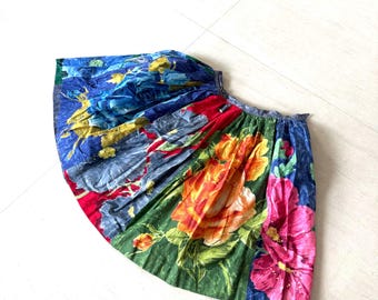Puede incluir: Una falda colorida con un estampado floral. La falda presenta grandes flores en tonos de rojo, naranja y rosa sobre un fondo verde. También se ven patrones florales azules y amarillos.