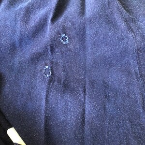 May include: Close-up of a dark blue fabric with two small holes. The fabric has a textured surface.