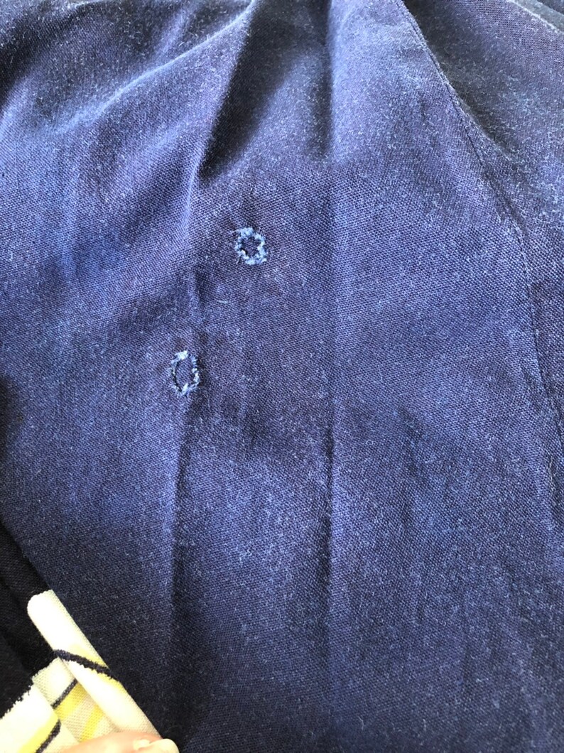 May include: Close-up of a dark blue fabric with two small holes. The fabric has a textured surface.