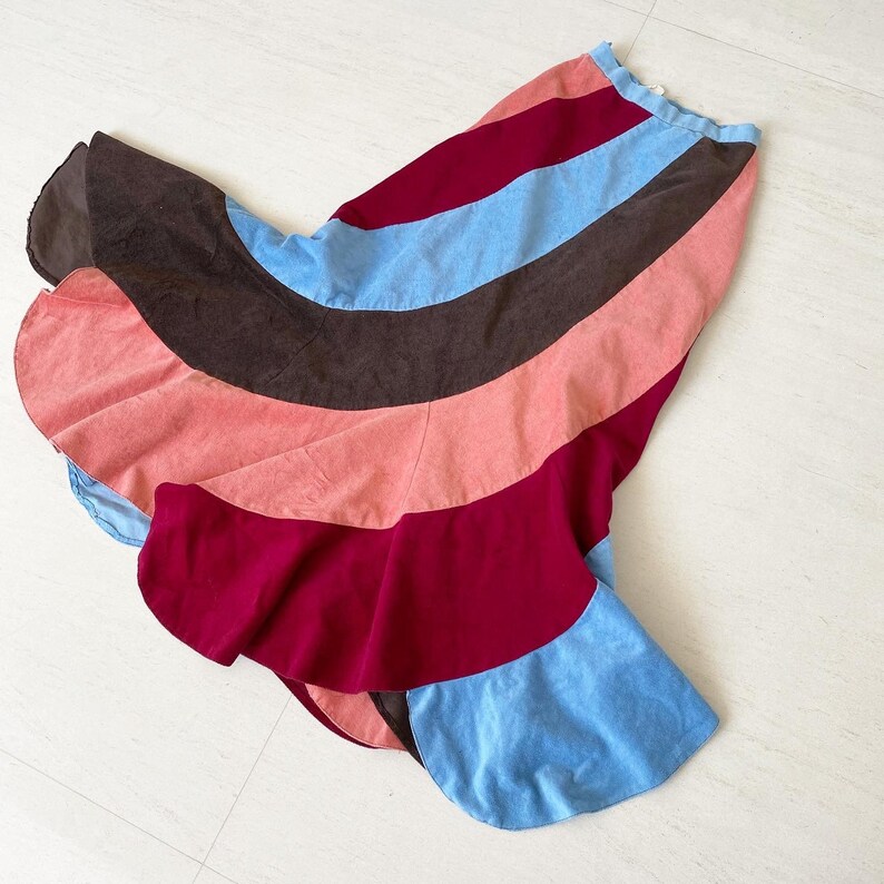 May include: A colorful, multi-colored skirt with a flared, A-line silhouette. The skirt is made of a soft, textured fabric and features a variety of colors, including brown, pink, red, and blue.