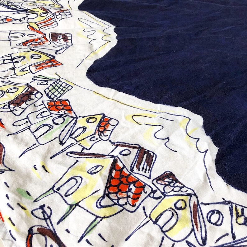 May include: A white fabric with a blue border and a repeating pattern of yellow, red, and blue houses. The houses are drawn in a simple, childlike style.