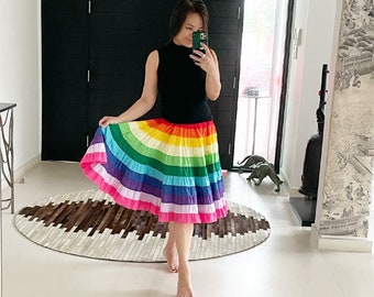 May include: A woman wearing a black sleeveless top and a rainbow-striped skirt. The skirt is made of a soft, flowing fabric and has a tiered design. The woman is standing in front of a mirror and is looking at herself.