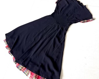 May include: A navy blue dress with short sleeves and a flared skirt. The hem and sleeve edges feature a colorful plaid pattern in red, yellow, and green. The dress has a fitted waist and a flowing skirt.