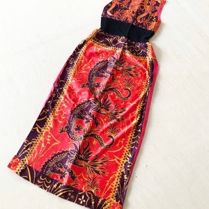 May include: A long red and gold dress with a black bodice and a dragon print. The dress has a sleeveless design and a high neckline.