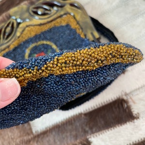 May include: A beaded purse with a blue and gold design. The purse is made of small, round beads that are sewn together to create a textured surface. The purse has a gold trim and a small, round handle.