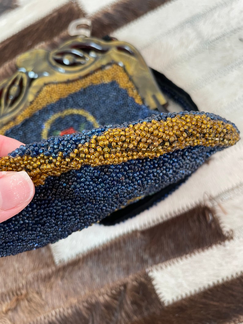 May include: A beaded purse with a blue and gold design. The purse is made of small, round beads that are sewn together to create a textured surface. The purse has a gold trim and a small, round handle.