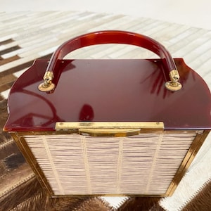 Könnte beinhalten: Eine vintage rote Handtasche aus Kunststoff mit einem gewebten strohähnlichen Futter und einem braunen Schildpattgriff. Die Tasche hat goldfarbene Beschläge.