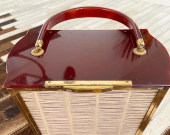 May include: A vintage red plastic handbag with a woven straw-like lining and a brown tortoise shell handle. The bag has gold-toned hardware.