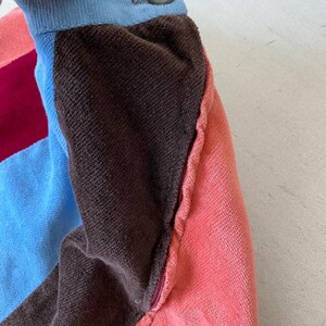 May include: Close-up of a multi-colored fabric with a zipper. The fabric is brown, pink, blue, and burgundy. The zipper is silver and is sewn into the fabric.