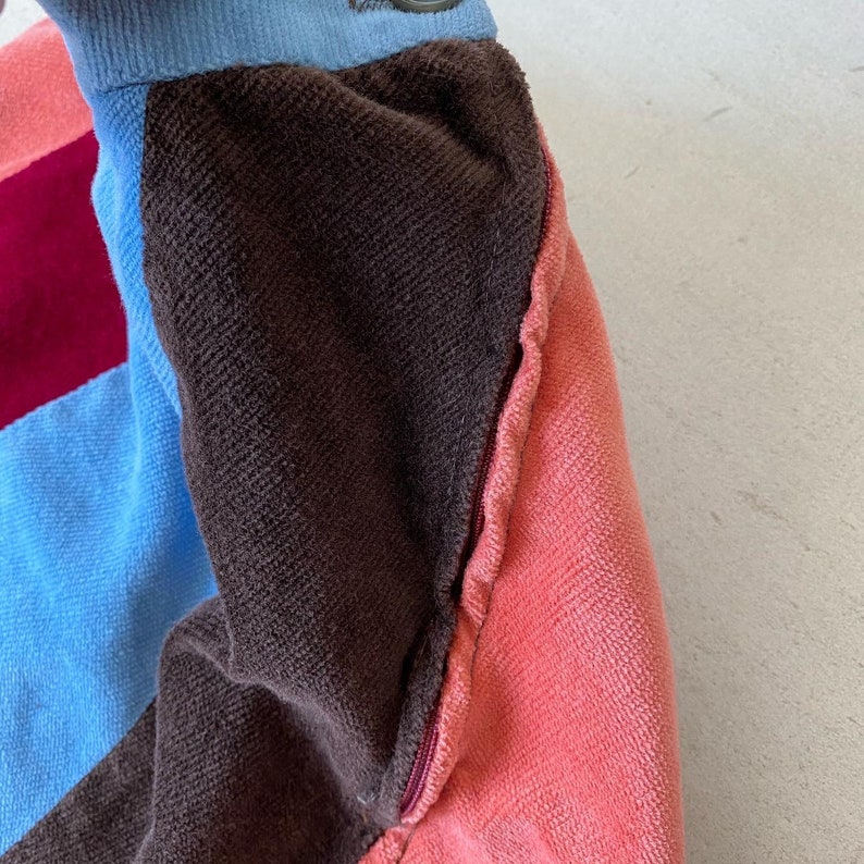 May include: Close-up of a multi-colored fabric with a zipper. The fabric is brown, pink, blue, and burgundy. The zipper is silver and is sewn into the fabric.