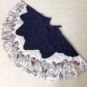 May include: A navy blue skirt with a white and yellow print of houses and boats. The skirt is full and has a gathered waist.
