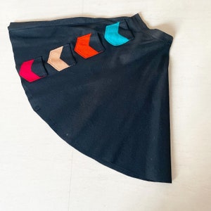 Op de afbeelding: Een zwarte rok met een gebogen zoom en kleurrijke pijlvormige pleisters die aan de zijkant zijn genaaid.