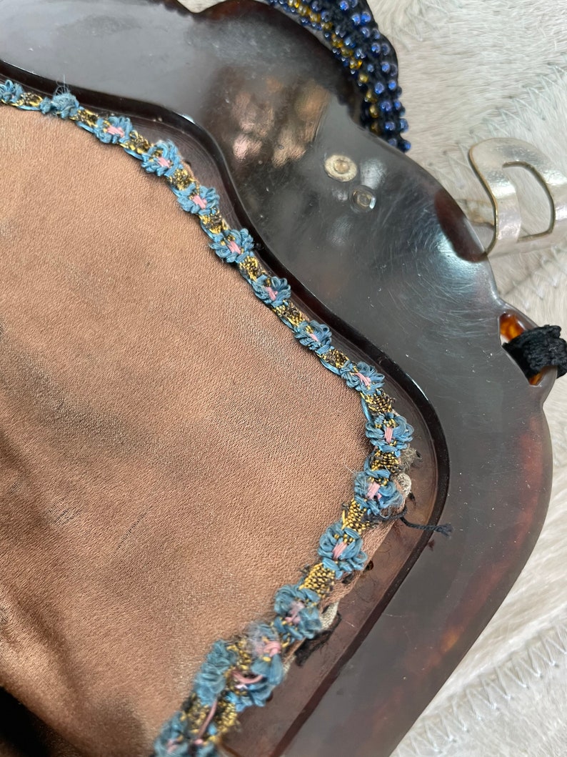 May include: A vintage tortoiseshell compact mirror with a blue and gold trim. The mirror has a brown velvet lining.