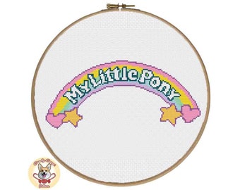 Peut inclure: Un cercle de broderie au point de croix avec un motif arc-en-ciel et le texte "My Little Pony". L'arc-en-ciel est composé de nuances de jaune, de rose et de bleu, avec des cœurs roses et des étoiles jaunes. Le cercle est en bois.