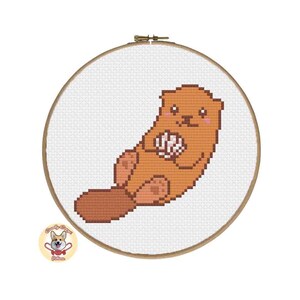May include: A cross-stitch pattern of a brown and white cartoon otter holding a pink seashell. The otter is sitting on its tail and has a happy expression.