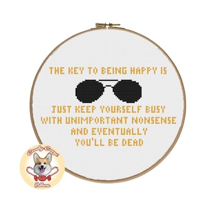 May include: White embroidery hoop with a black and white cross-stitch design that reads "THE KEY TO BEING HAPPY IS JUST KEEP YOURSELF BUSY WITH UNIMPORTANT NONSENSE AND EVENTUALLY YOU'LL BE DEAD". The design includes a pair of black sunglasses. A small, round sticker with a cartoon corgi dog is in the lower left corner.