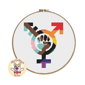 Puede incluir: Un patrón de punto de cruz que presenta un símbolo de género con un puño levantado en el centro. El símbolo está rodeado por un arcoíris de colores, incluyendo rojo, naranja, amarillo, verde, azul, añil y violeta. El puño es negro y marrón, representando el movimiento Black Lives Matter.