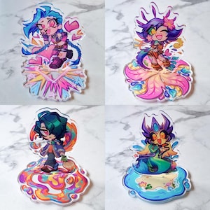 May include: Four acrylic character charms with anime-style illustrations. Each charm shows a different character with bright hair and clothing, set on a decorative base. The charms display various poses and expressions, with vivid colours.
