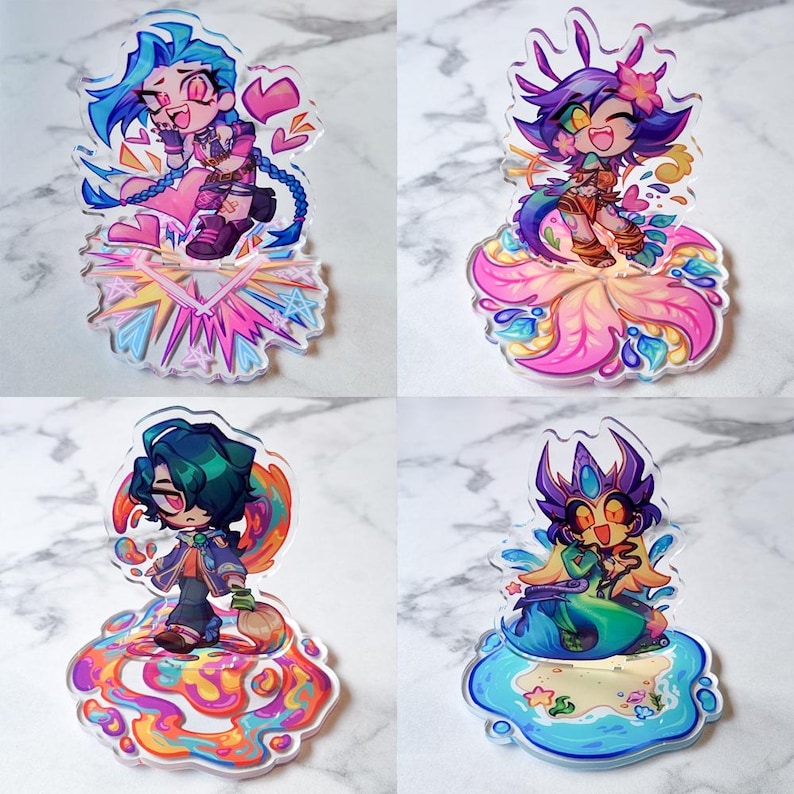 May include: Four acrylic character charms with anime-style illustrations. Each charm shows a different character with bright hair and clothing, set on a decorative base. The charms display various poses and expressions, with vivid colours.