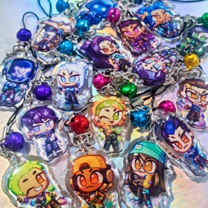 May include: A selection of clear acrylic keychains with cartoon characters in various colours. Each keychain has a unique design, attached to a silver chain with a decorative bead. The keychains are of various sizes and shapes, suitable for attaching to keys or bags.