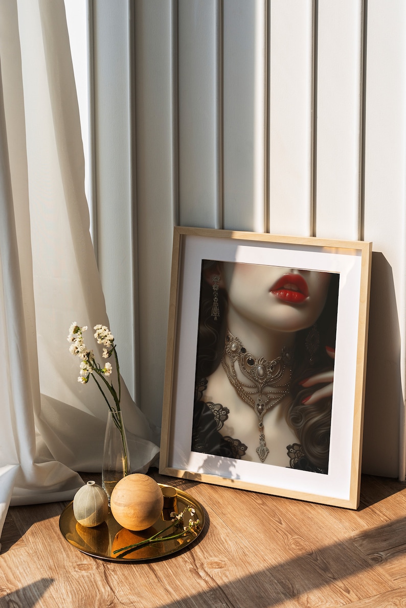 Puede incluir: Una impresi&oacute;n enmarcada de la cara de una mujer con l&aacute;piz labial rojo y un collar de oro grande. La impresi&oacute;n est&aacute; en un marco de madera y se apoya contra una pared blanca.