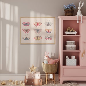 K&ouml;nnte beinhalten: Ein gerahmter Druck einer Sammlung bunter Schmetterlinge in einem Farbschema aus Rosa, Wei&szlig; und Grau. Der Druck h&auml;ngt an einer hellbeigen Wand in einem Raum mit einem rosa B&uuml;cherregal und einem Weidenkorb.
