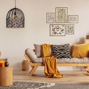 K&ouml;nnte beinhalten: Ein helles Holz-Futon-Sofa mit einer gelben Wolldecke und schwarzen und wei&szlig;en Kissen mit Mustern. Das Sofa steht in einem Wohnzimmer mit einem Holz-Beistelltisch, einem gewebten Wandteppich und gerahmten Drucken von Schmetterlingen und Pflanzen.