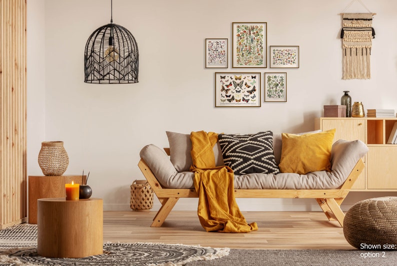 K&ouml;nnte beinhalten: Ein helles Holz-Futon-Sofa mit einer gelben Wolldecke und schwarzen und wei&szlig;en Kissen mit Mustern. Das Sofa steht in einem Wohnzimmer mit einem Holz-Beistelltisch, einem gewebten Wandteppich und gerahmten Drucken von Schmetterlingen und Pflanzen.