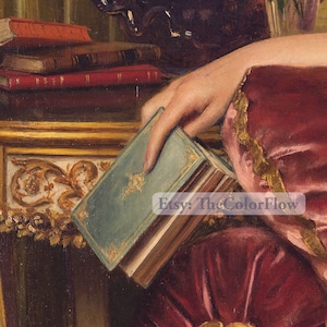May include: A woman's hand holds a closed book with a teal blue cover and gold accents. The book is resting on a table with a gold and ornate design. The woman is wearing a red and gold dress.