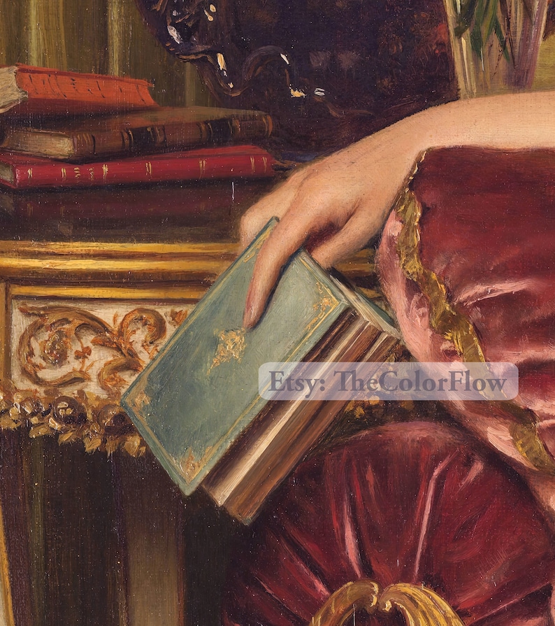May include: A woman's hand holds a closed book with a teal blue cover and gold accents. The book is resting on a table with a gold and ornate design. The woman is wearing a red and gold dress.