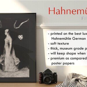 May include: A black and white print of a woman in a long dress with a mask and horns above her head. The print is framed and hanging on a wall. The text "Hahnem&uuml;hle FINEART" is printed on the wall below the frame. The text below the FINEART logo reads: "printed on the best luxury paper: Hahnem&uuml;hle German Etching soft texture thick, museum grade paper will keep shape when framed premium as compared to poster papers"