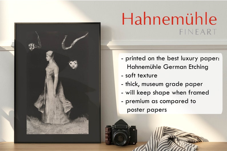 May include: A black and white print of a woman in a long dress with a mask and horns above her head. The print is framed and hanging on a wall. The text "Hahnem&uuml;hle FINEART" is printed on the wall below the frame. The text below the FINEART logo reads: "printed on the best luxury paper: Hahnem&uuml;hle German Etching soft texture thick, museum grade paper will keep shape when framed premium as compared to poster papers"
