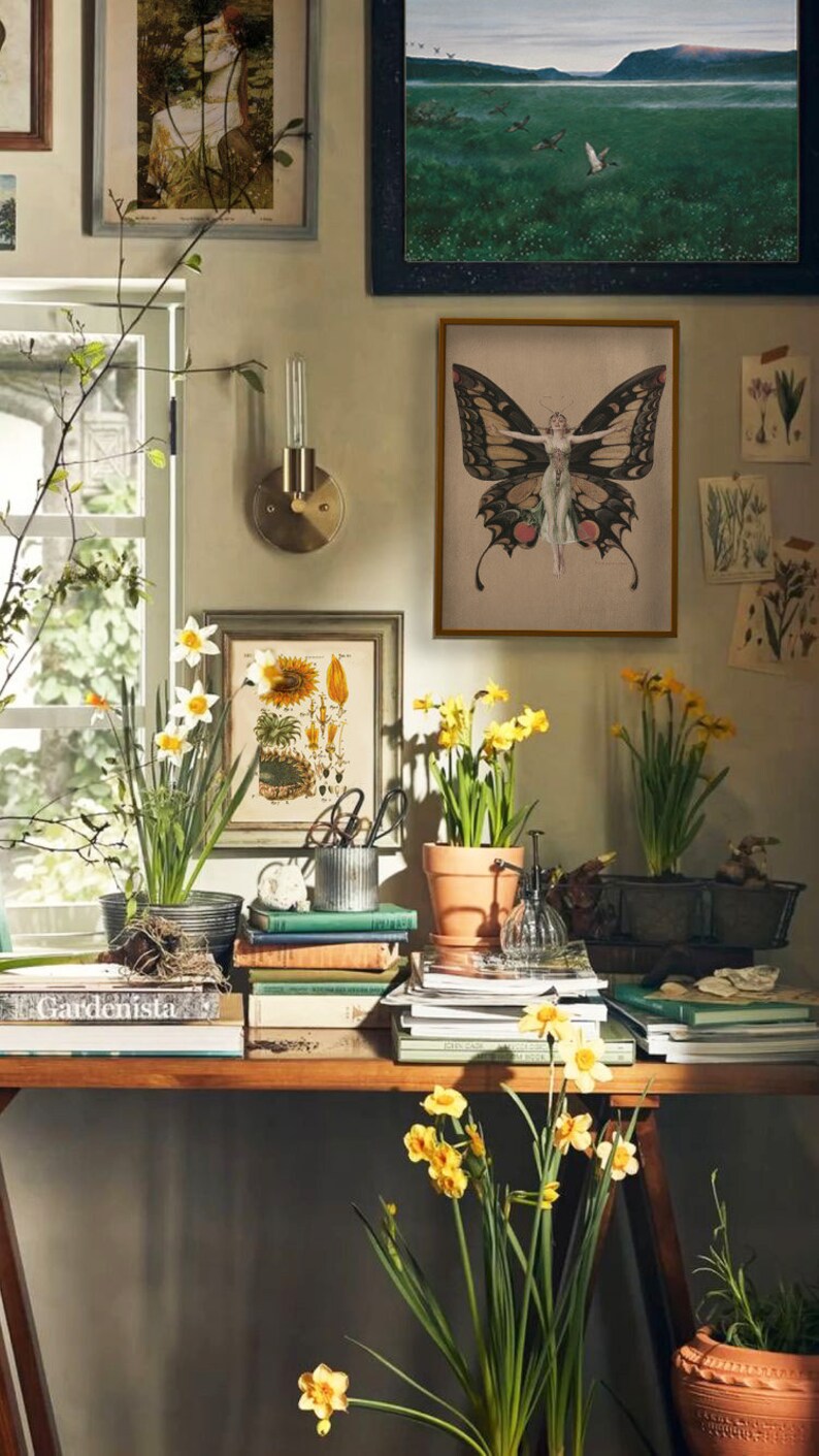 Pode incluir: Uma natureza morta com uma cole&ccedil;&atilde;o de impress&otilde;es bot&acirc;nicas vintage, uma impress&atilde;o emoldurada de uma mulher com asas de borboleta e narcisos em vaso. As impress&otilde;es s&atilde;o exibidas em uma parede com uma prateleira de madeira abaixo, que est&aacute; cheia de livros e outros itens decorativos.