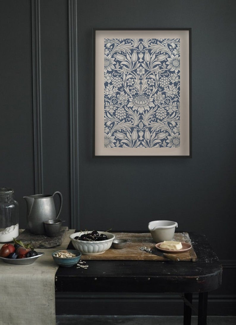 May include: A framed print of a vintage floral pattern in shades of blue and white. The print features a repeating design of stylized flowers, leaves, and vines. The frame is black and has a white mat.