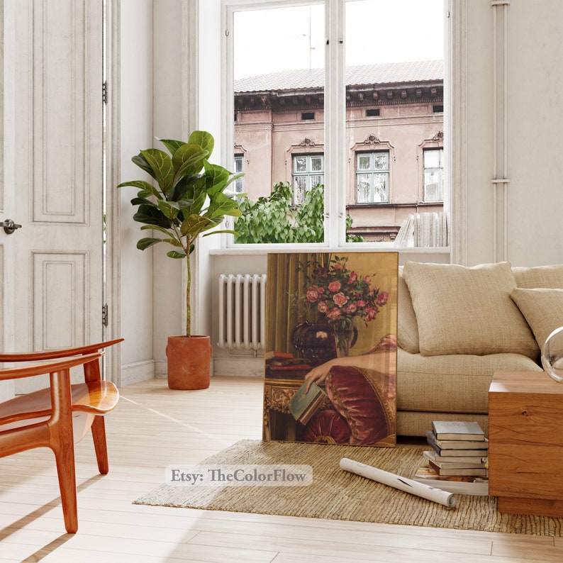May include: A vintage-style painting of a woman in a red dress holding a book. The painting is framed and hanging on a wall in a living room setting. The woman is sitting in a chair with a bouquet of pink roses in a vase behind her.