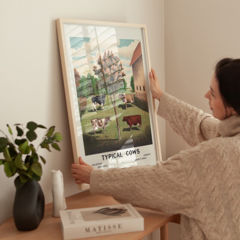 May include: A framed poster with a vintage illustration of different breeds of cows in a field. The poster is titled "Typical Cows" and lists the breeds: Holstein, Ayrshire, Jersey, Short-Horn.