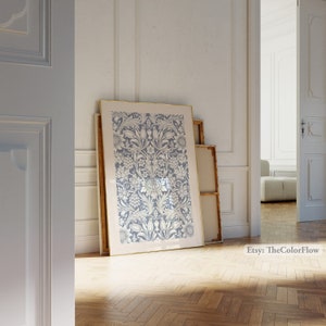 May include: A framed print of a blue and white floral pattern. The print is in a gold frame and is leaning against a white wall.