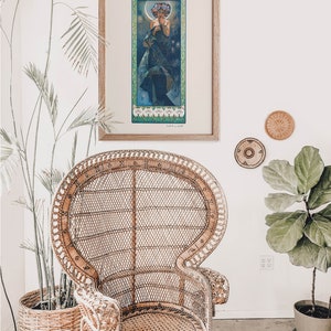 Puede incluir: Una impresi&oacute;n de arte vintage enmarcada de una mujer con un vestido azul fluido y una corona de flores. La impresi&oacute;n est&aacute; en un marco de madera y est&aacute; colgada en una pared blanca.
