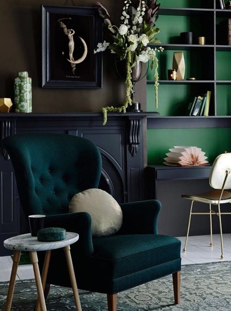 Puede incluir: Un sill&oacute;n de terciopelo verde oscuro con un coj&iacute;n beige claro se encuentra en una habitaci&oacute;n con paredes verde oscuro y una chimenea negra. Una mesa peque&ntilde;a con una tapa de m&aacute;rmol blanco se encuentra frente al sill&oacute;n.